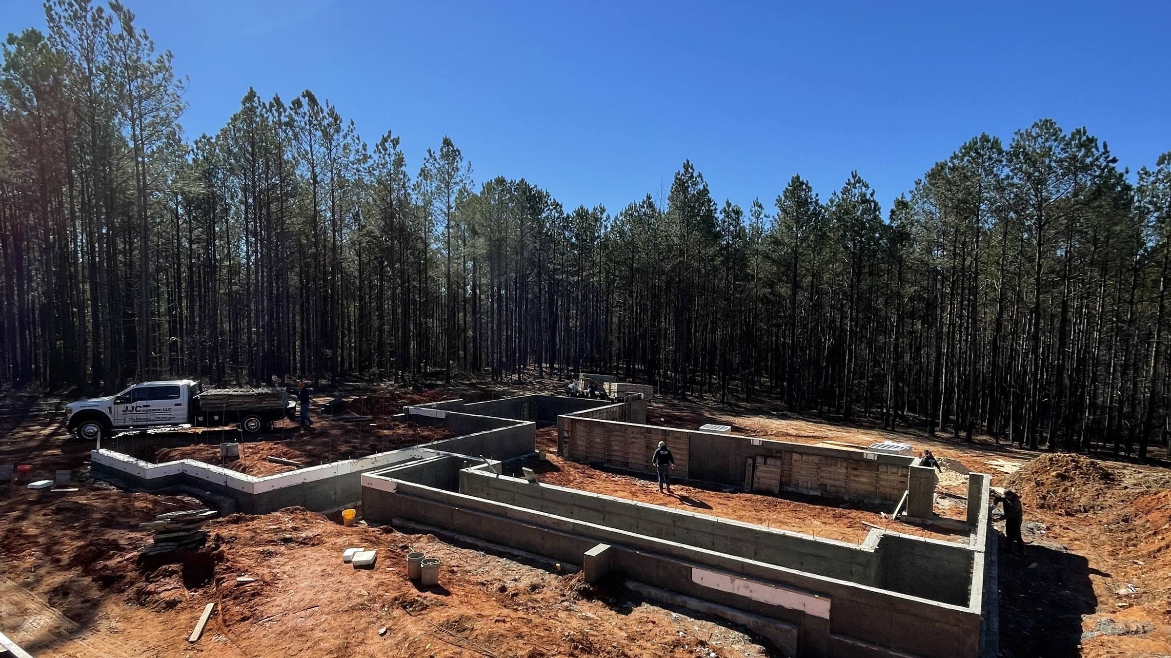 Poured concrete foundation walls on a cleared lot, form panels in the foreground